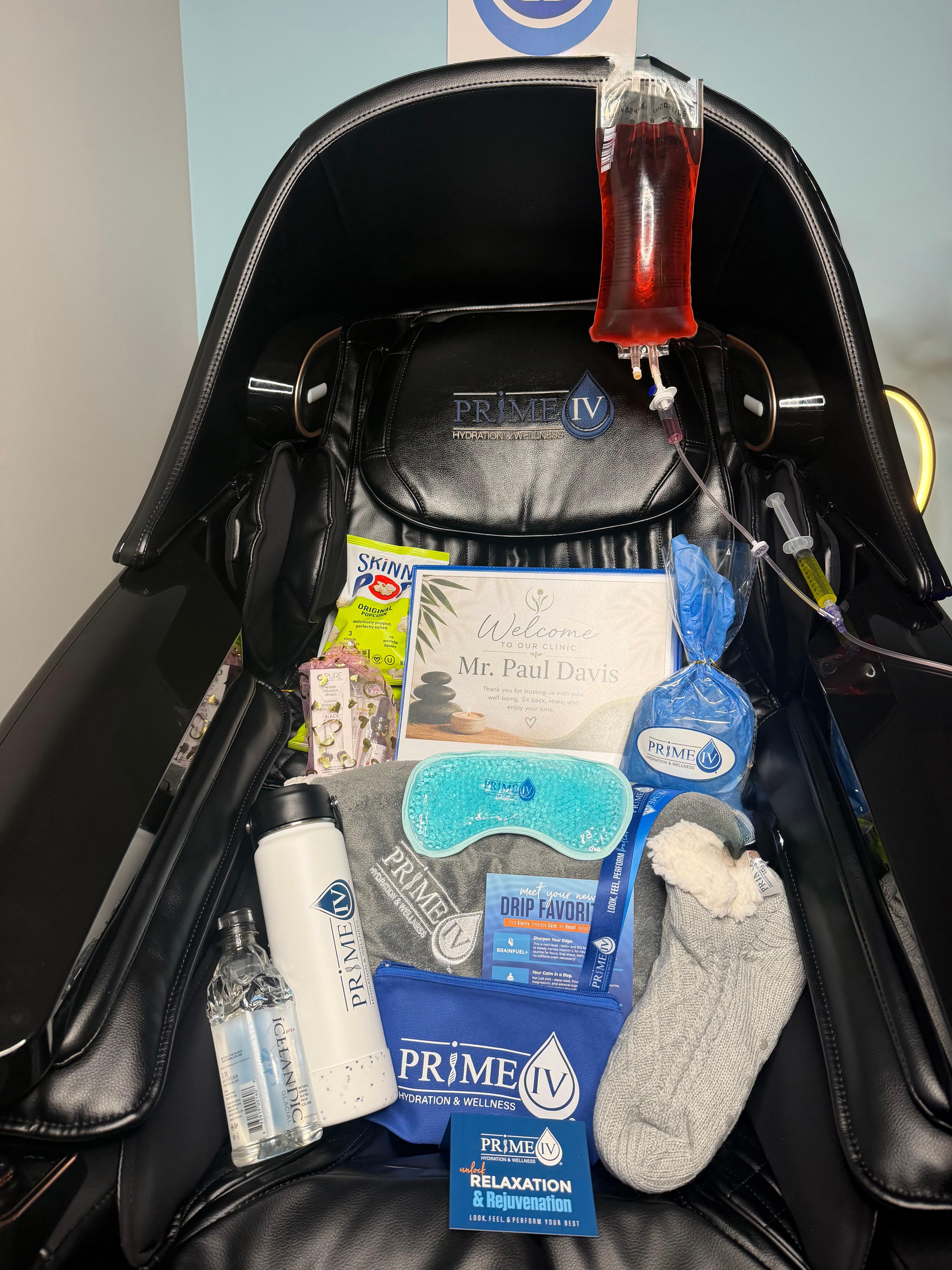 Personalized Prime IV welcome gift set with branded water bottle, eye mask, cozy socks, and a welcome card waiting on a treatment chair